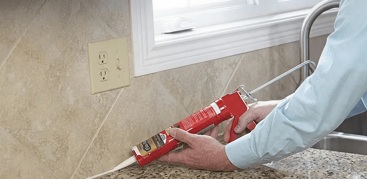 Handyman applying caulk along a kitchen backsplash and countertop seam in Huntsville, AL
